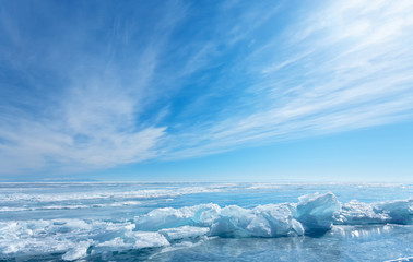 Winter landscape of the frozen Baikal Lake. Beautiful layered clouds over the Small Sea Strait and endless fields of blue ice with cracks. Cold natural background