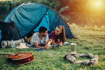 young couple enjoying camping outdoor by the river - obrazy, fototapety, plakaty