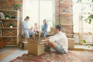 New life. Adult family moved to a new house or apartment. Spouses and children look happy and confident. Moving, relations, new life concept. Playing together, sitting near by window and laughting.