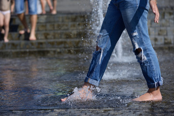 Strong heat in the city: girl’s leg playing with fountain water jets at the square