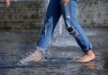 Strong heat in the city: girl’s leg playing with fountain water jets at the square