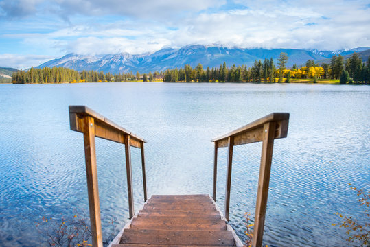 peque&ntilde;o puente de madera en el largo maligne con agua azul turquesa, un cielo azul, nubes grises, un bosque de pinos verdes y amarillos que se localiza en el parque nacional de Jasper Alberta Canad&aacute; 
