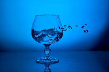 Clear water splash in glass with drops on blue lighting background
