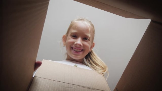 Surprised girl unpacking and opening carton box and looking inside. Child emotions concept.