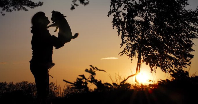 A woman kisses her dog on a sunset background. Silhouette of a woman and a dog. Pet love
