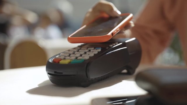 Close up hands woman paying in the cafe by credit card swiping with credit card on pos payment terminal on table in sunlight customer machine money terminal cash client electronic slow motion
