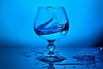 Pure fresh ice cold water splash in dinking glass with drops on blue lighting background