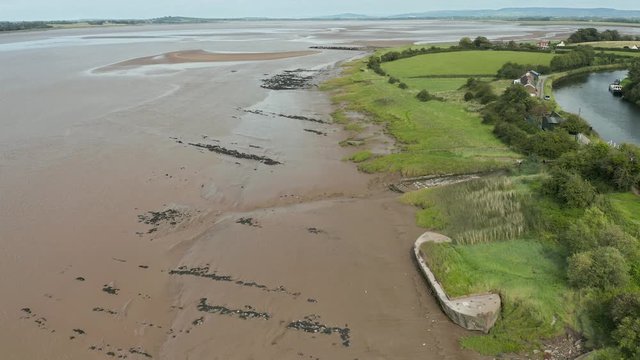 Aerial drone view of old hulks of shipwrecks on the banks of a large,brown river (Purton Hulks, River Severn, England)