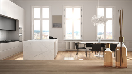 Wooden table top or shelf with aromatic sticks bottles over blurred modern white kitchen with parquet floor and dining table, white architecture interior design