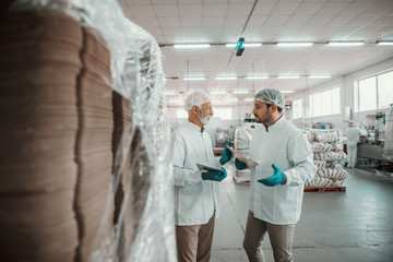 Two Caucasian supervisors with serious facial expression dressed in white sterile uniforms talking...