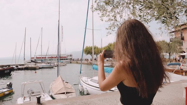 Young girl filming making pictures of a lake with yachts and boats on summer august day sunny at torre del benaco veneto italy 2019