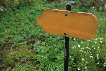 Empty yellow wooden sign board in garden, blank for text.