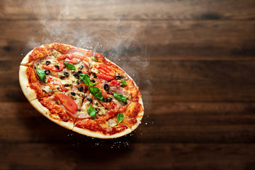 Pizza on a wooden background with ham, olives, tomatoes and green basil. Itolyan cuisine, copy space.