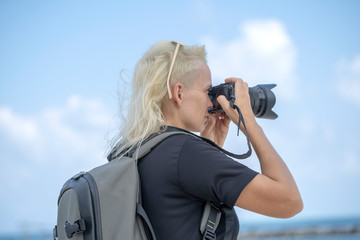 Tourist traveler photographer taking pictures of landscape on photo camera , hipster girl with backpack enjoying beautiful sea landscape. Close up portrait young tourist of a blonde girl