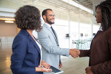 Cheerful business people shaking hands. Businesswoman holding digital tablet and looking at smiling business colleagues shaking hands in office. Cooperation concept