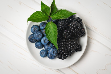 Top view ripe blackberries and blueberries in a white dish on a wooden table