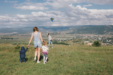 Happy family flying a colorful kite on green meadow.