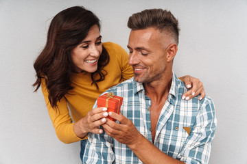 Happy cheerful woman give a present to her man isolated over grey wall background.