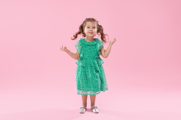 Funny little kid, toddler girl in fashionable green dress isolated on pink background
