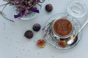 Homemade fig jam in glass jar with fresh purple figs on gray wooden background. Soft focus. Harvesting time or healthy food concept. Top view