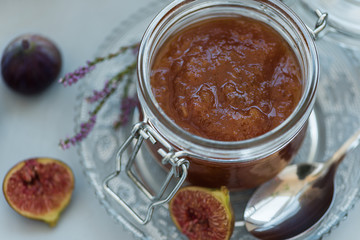 Close up homemade fig jam in glass jar with fresh purple figs on gray wooden background. Soft focus. Harvesting time or healthy food concept