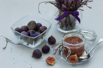 Homemade fig jam in glass jar with fresh purple figs on gray wooden background. Soft focus. Harvesting time or healthy food concept