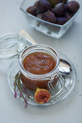 Homemade fig jam in glass jar with fresh purple figs on gray wooden background. Soft focus. Harvesting time or healthy food concept