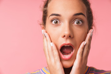 Image closeup of surprised young woman dressed in colorful clothes screaming and touching her cheeks