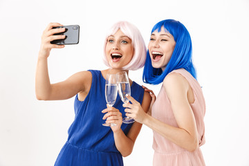 Portrait of two funny women wearing blue and pink wigs taking selfie photo on cellphone while drinking champagne