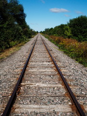 Fototapeta premium Railway tracks in a rural scene with a bright blue sky and white clouds. Tracks disappear into the distance.