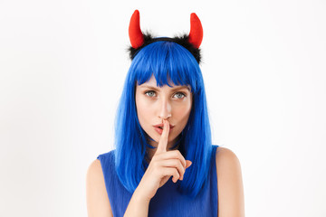 Portrait of young nice woman wearing blue wig and toy devil horns gesturing silence sign
