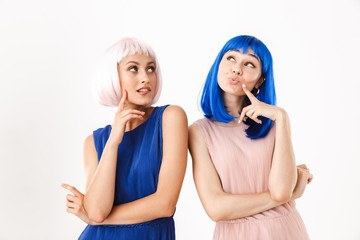 Portrait of two nice women wearing blue and pink wigs dreaming while looking upward at copyspace