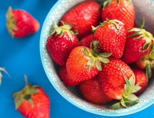 Fototapeta na wymiar bright printed bowl of fresh strawberries on blue wooden background