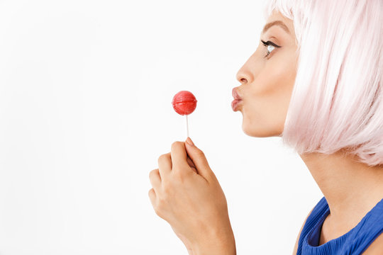 Photo in profile of joyful happy woman wearing pink wig holding lollipop and making kiss face