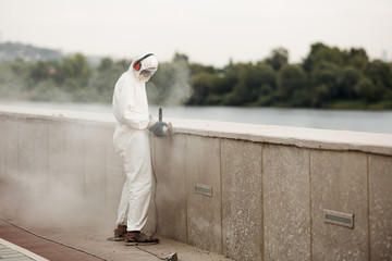 A man in a white protective suit and respirator grinds the concrete slabs of the waterfront