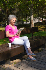Peaceful inspired old lady enjoying novel in park. Senior grey haired woman in casual with coffee...