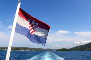 Flag of Croatia blowing in the wind. Croatian coast and islands in the background.