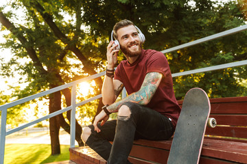 Attractive cheerful young man sitting at the skate park ramp