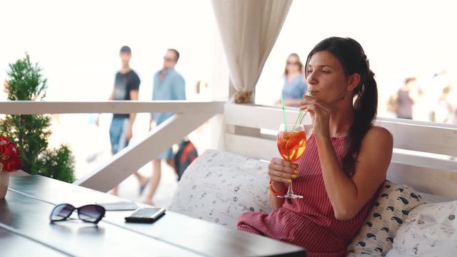 Beautiful girl chilling in cafe on the seashore and enjoying cocktail in summer weekend. Video shot of people on vacation in 4K definition