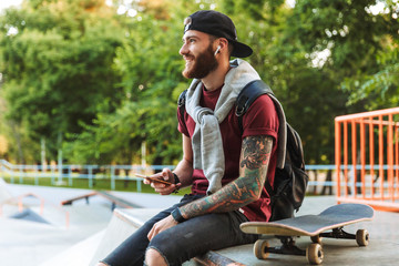Attractive cheerful young man sitting at the skate park ramp