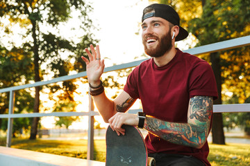 Attractive cheerful young man sitting at the skate park ramp