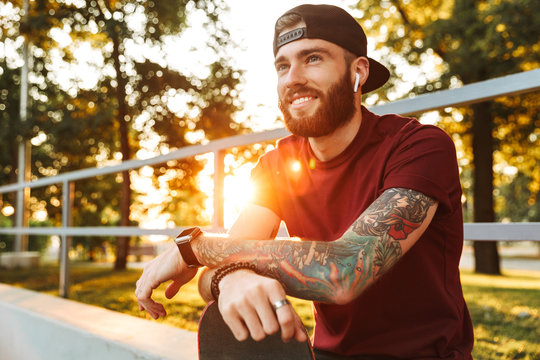 Attractive cheerful young man sitting at the skate park ramp