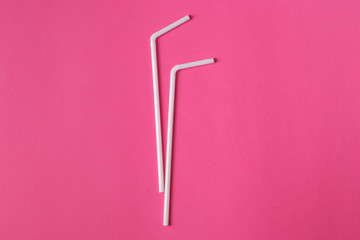 Two white plastic straws on pink background