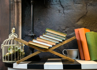 Stacked books on resting wood stand next to wall. Education concept.