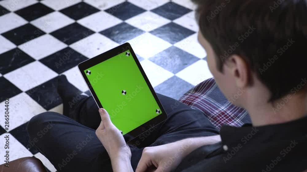 Poster view from the shoulder of young man in black shirt using green mock-up screen digital tablet compute