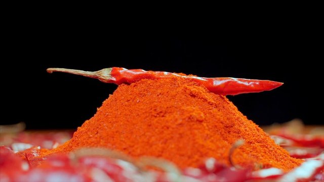 Shot of dried red chilly dropping on the heap of chilly powder. 