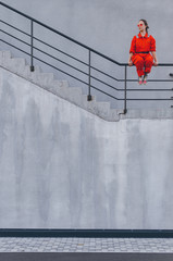 Young woman in red overalls and red sunglasses posing on the gray stairs. Industrial concept