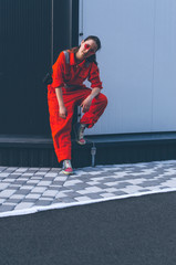 Young woman in red overalls and red sunglasses posing near grey and black wall. Industrial concept