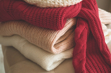 Obraz na płótnie Canvas A stack of knitted sweaters in the interior of the living room. The concept of autumn winter comfort