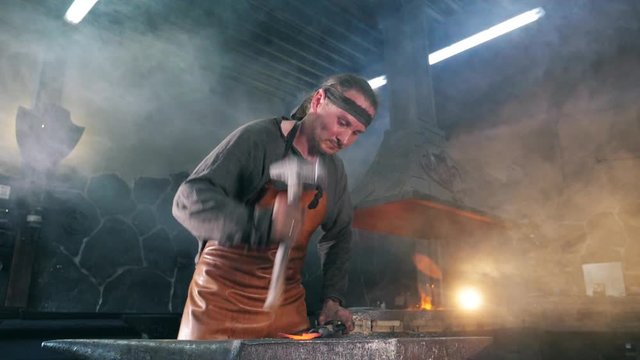 Male forger is striking metal with a hammer in slow motion